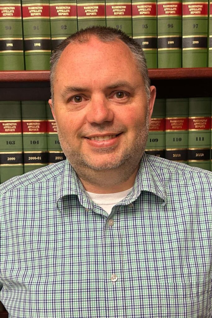Smiling person in checkered shirt with law books background.